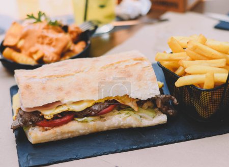 Foto de Delicioso sándwich de lomo de ternera con jamón y queso, acompañado de papas fritas - Imagen libre de derechos