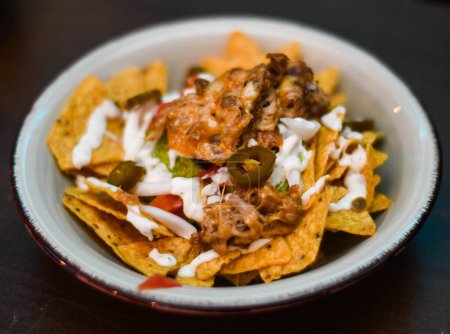 Serving of nachos with meat, cheese, white sauce and jalapenos