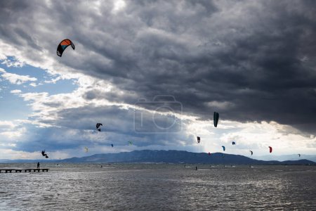 Foto de Un montón de kitesurfistas en el mar con nubes dramáticas antes de la lluvia, kitesurfistas en la playa de trabucador en Delta del Ebro - Imagen libre de derechos