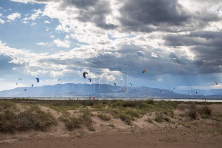Téléchargez les photos : Beaucoup de kitesurfers dans la mer avec des nuages spectaculaires avant la pluie, kitesurfers sur la plage de trabucador à Delta del Ebro - en image libre de droit