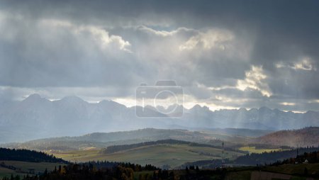 Photo for Sunlit foothills. In the distance you can see the Tatra Mountains. Storm clouds on the mountain peaks - Royalty Free Image
