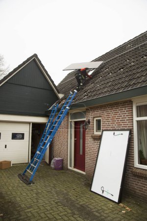 Téléchargez les photos : Travailleur installant des panneaux solaires sur le toit - en image libre de droit