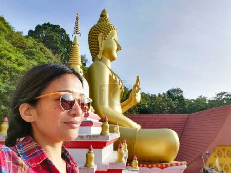 Foto de Una joven tailandesa tomando una selfie frente a una estatua de Buda en Wat Khao Rang, un templo budista en Phuket, Tailandia. - Imagen libre de derechos