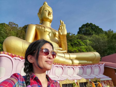 Foto de Una joven tailandesa tomando una selfie frente a una estatua de Buda en Wat Khao Rang, un templo budista en Phuket, Tailandia. - Imagen libre de derechos