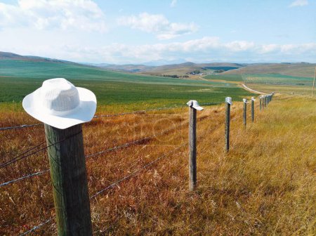 Foto de Sombrero de vaquero en el poste de la cerca en un campo de tierras de cultivo situado entre las Montañas Rocosas y la pradera canadiense, en el país de alta ganadería de Alberta, es el histórico Camino de los Vaqueros. Esta ruta panorámica a lo largo de la carretera 22. - Imagen libre de derechos