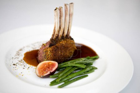 Roasted spring lamb rack with fig and green beans on a white dish.