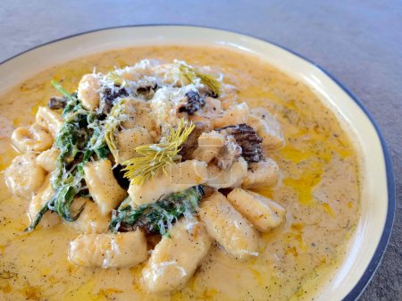 Gnocchi avec une sauce faite de champignons de morilles sauvages fourragés, orties sauvages, pointes de sapin mariné et sauce au beurre de pissenlit sur une assiette blanche avec de l'espace de copie en arrière-plan.