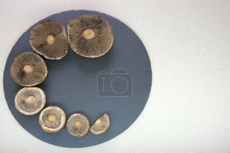 Téléchargez les photos : Mushrooms Champignons lie on a round, black board on the table, in the kitchen. The idea of dietary, healthy eating. Low-calorie food. High quality photo - en image libre de droit