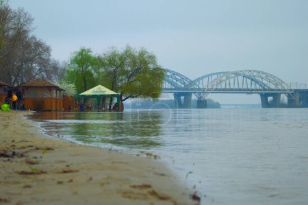 Téléchargez les photos : Kiev, Ukraine-16 avril 2023 : Vue du paysage des hautes eaux à Kiev, printemps 2023. Une partie de la plage de sable avec des belvédères est inondée. Les gens se reposent. Inondation de la rivière Dipro. Météo brumeuse et pluvieuse. - en image libre de droit