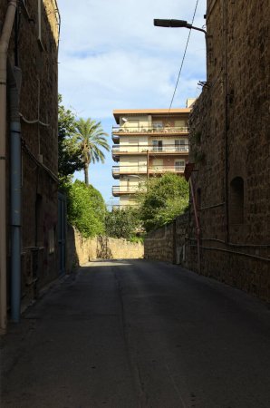 Photo for Narrow asphalt road between two stone old residential houses in Santo Stefano di Camastra, Sicily, Italy. High-rise building in the background. Travel and tourism concept. - Royalty Free Image