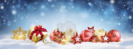 Téléchargez les photos : Fond enneigé d'hiver avec des jouets de Noël, des dérives de neige, avec une belle lumière et des flocons de neige sur le ciel bleu en soirée, format bannière, espace de copie. Décoration de Noël. - en image libre de droit