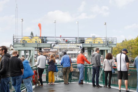 Photo for Friday Harbor, Washington, United States - 09-11-2021: A view of a ferry boat departing the dock of Friday Harbor. Several people stand on the outdoor deck level. - Royalty Free Image