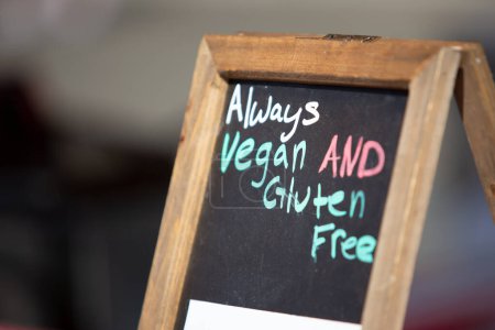 Téléchargez les photos : A view of a chalkboard sign letting customers know the food products are always vegan and gluten free. - en image libre de droit