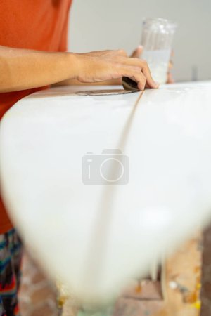 Vertical close-up of a man repairing and sanding a surfboard in a shop