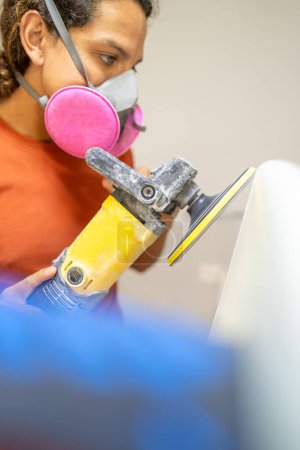 Vertical close-up photo of an accurate worker grinding a surfboard with electric disc