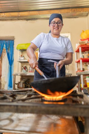 Latin female chef removing ingredients form a frying pan in a commercial peruvian kitchen