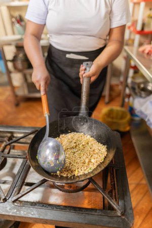 Vertical Primer plano de las manos de un chef que prepara arroz chaufa en una cocina comercial
