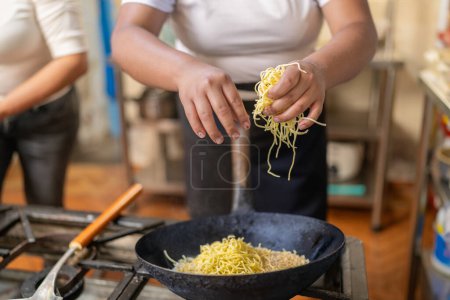 Chef cooking yellow noddles in a frying pan in a commercial kitchen