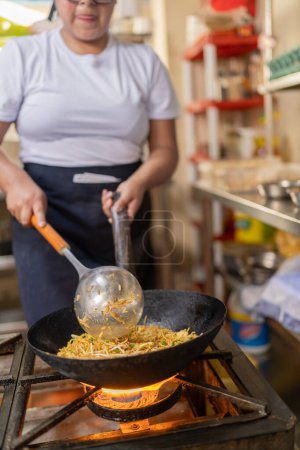 Photo recadrée verticale d'un chef professionnel latina sautant des nouilles aux légumes dans une casserole