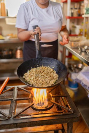 Vertical cropped photo of a chef using a pan sauteing noddles in a restaurant