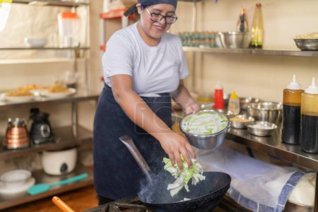 Smiling female cook adding vegetables to a frying pan in the restaurant