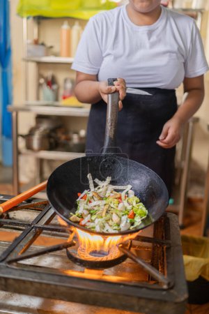 Vertical photo of a female chef cooking veggies in a wok pan in a restaurant