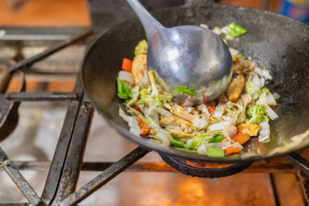 Wok frying pan with vegetables and chicken on stove in a restaurant