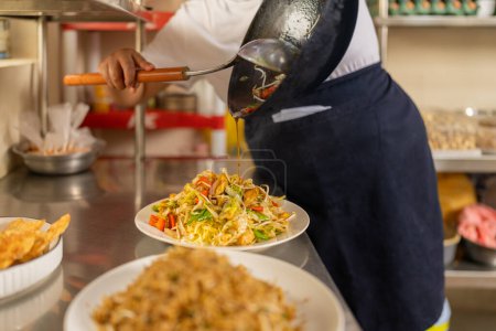 Cook plating vegetables noddles in the counter of a kitchen in a peruvian restaurant
