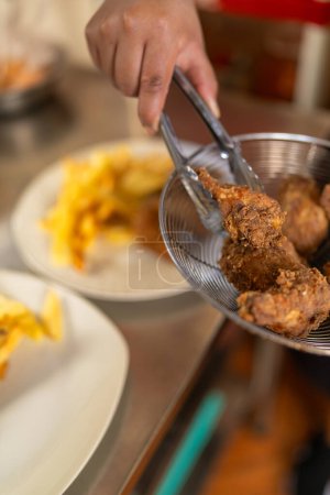 Photo for Vertical close-up photo of a cook removing breaded chicken from the pan to plate it - Royalty Free Image
