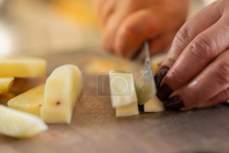 Close-up of the hands of a female cook chopping potatoes in the counter of a kitchen