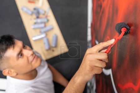 Top view horizontal photo of a latin young male muralist using a small roller to paint an urban mural
