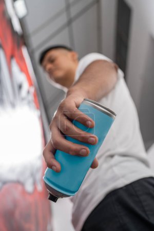 Vertical photo with focus on the hand of a latin vandal holding a spray while painting a graffiti on a wall