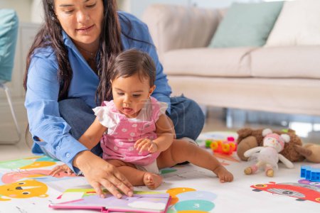 A mother guides her baby through an educational book, fostering learning and development during playtime on a colorful mat.