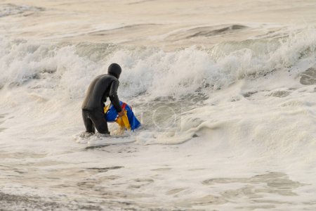 Vista trasera de un joven pescador latino saliendo del mar con una bolsa después de pescar con red