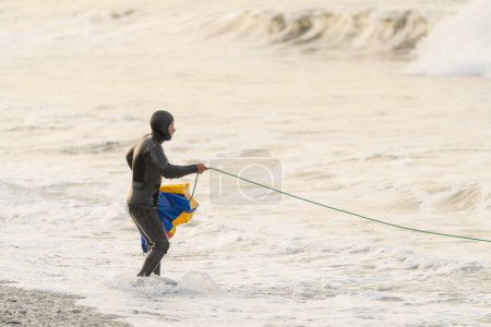 Pescador en traje de neopreno trabajando la pesca con la red de pie en el borde del agua de mar