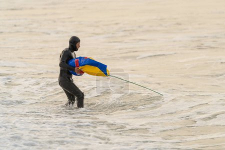 Pescador en traje de neopreno dentro del agua llevando una bolsa después de pescar con red