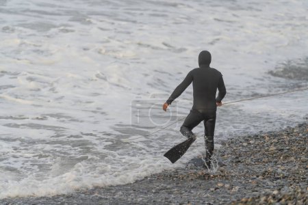 Rear view of an unrecognizable man in wetsuit and flippers entering into the sea water
