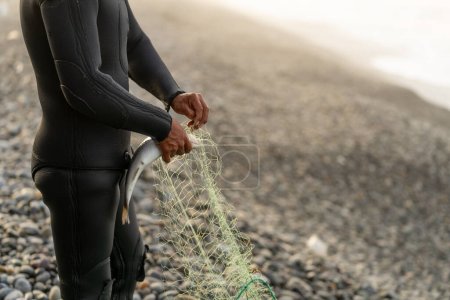 Horizontal photo with copy space and focus on a fisherman in wetsuit unhooking a caught fish from the net