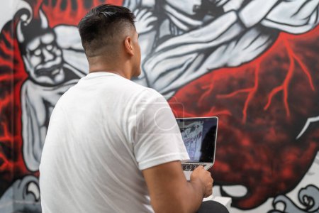 Pintor callejero usando un portátil para trabajar en un nuevo mural en interiores