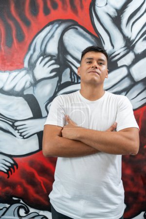 Vertical portrait of a latin male muralist standing proud with arms crossed in front of his work