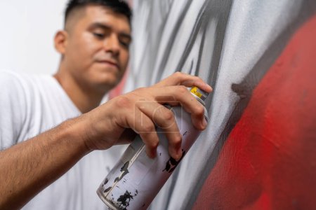 Low angle view close-up of a young male latin muralist painting a wall using spray