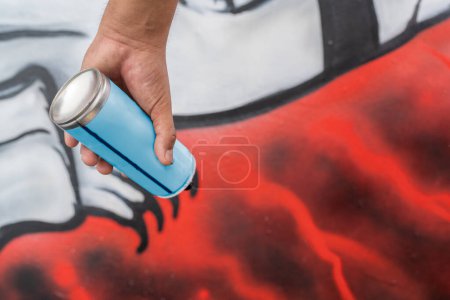 Mano de un artista callejero sosteniendo una lata de spray junto a un colorido mural