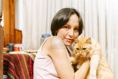 A cozy portrait of a woman affectionately holding her fluffy ginger cat, both looking into the camera.