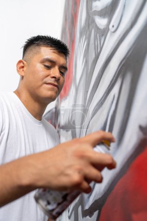 Foto vertical con foco en la cara de un joven artista latino concentrado que pinta una pared con aerosol