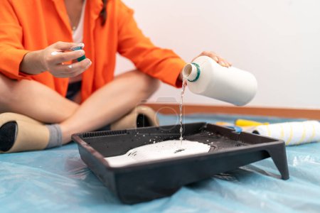 Foto de Mujer mezclando agua y pintura blanca en casa preparándose para pintar las paredes de la casa - Imagen libre de derechos