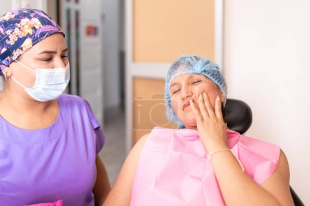 A seated patient gestures to her cheek while discussing discomfort with her attentive dentist in a clinic setting.