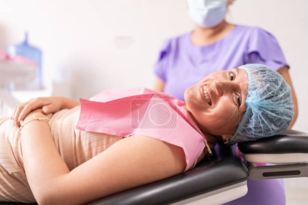 Eine Patientin liegt nach einem Eingriff lächelnd und entspannt im Zahnarztstuhl, während ihr Zahnarzt im Hintergrund bereit ist, zu helfen