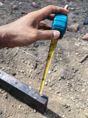 Téléchargez les photos : Builder utilise un ruban à mesurer pour trouver la distance entre le sol et le moule afin de trouver les coordonnées correctes pour préparer le sol en ciment. Fond flou - en image libre de droit