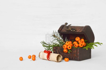 Téléchargez les photos : Composition de Noël de baies de rowan dans la poitrine vintage et rouleau de papier sur fond blanc - en image libre de droit