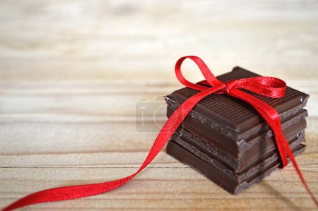 Foto de Envoltura de barras de chocolate con cinta roja sobre fondo de madera con espacio para copiar - Imagen libre de derechos
